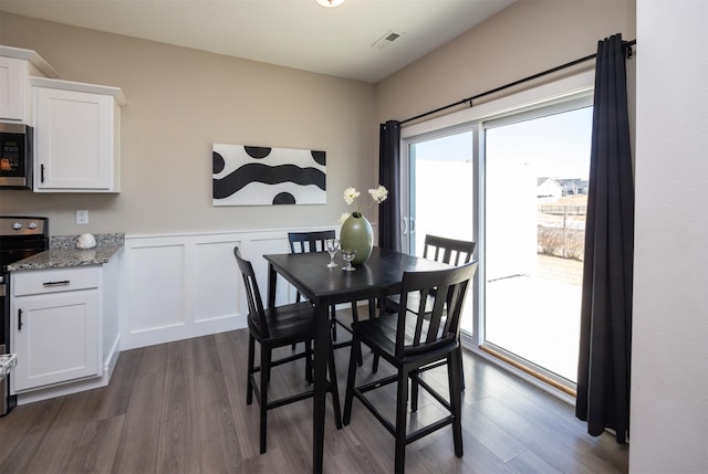 dining area with dark wood-style flooring, a wainscoted wall, a decorative wall, and visible vents