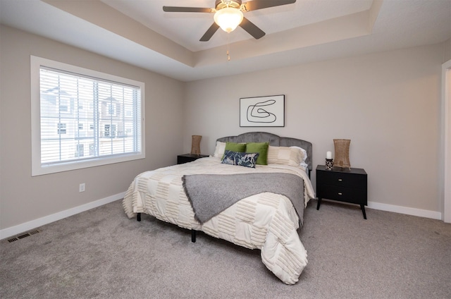 bedroom with light colored carpet, a ceiling fan, visible vents, baseboards, and a tray ceiling