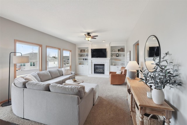 living area with a ceiling fan, a glass covered fireplace, built in features, and carpet