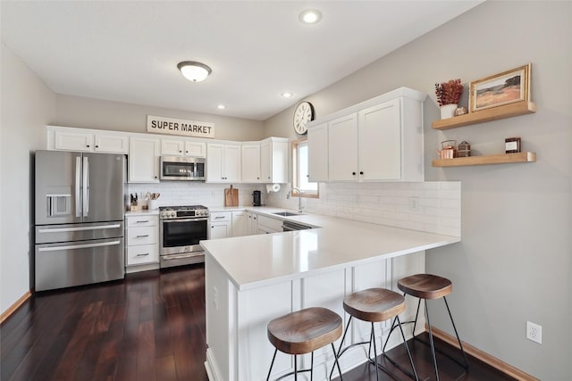 kitchen with appliances with stainless steel finishes, light countertops, white cabinets, and a peninsula