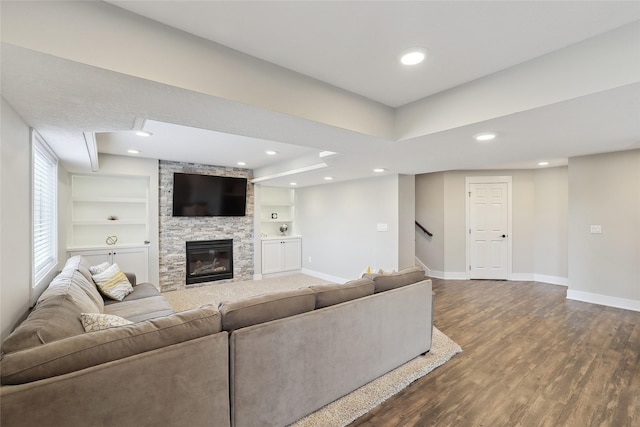 unfurnished living room with a stone fireplace, built in shelves, recessed lighting, dark wood-style flooring, and baseboards