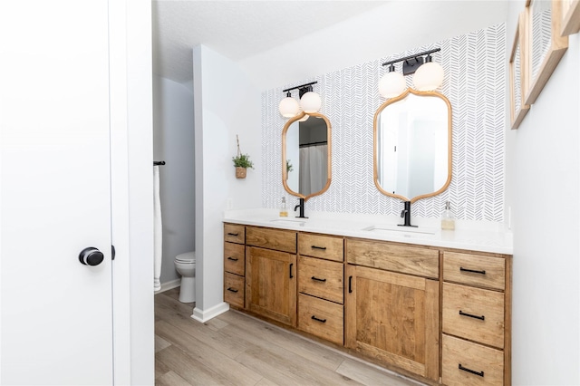 full bath featuring double vanity, wood finished floors, a sink, and toilet