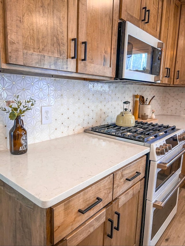 kitchen with range with two ovens, stainless steel microwave, brown cabinetry, and decorative backsplash