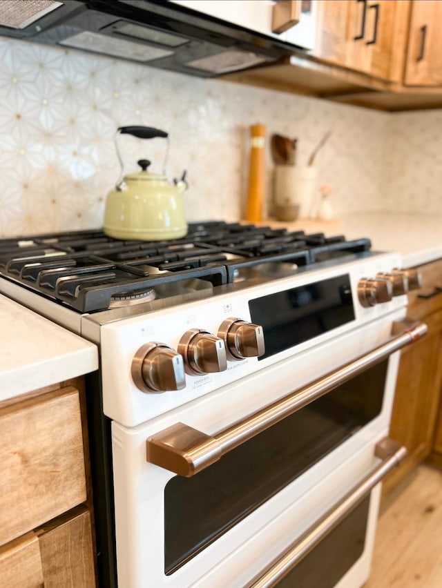 kitchen with light wood finished floors, tasteful backsplash, range with two ovens, brown cabinets, and light countertops