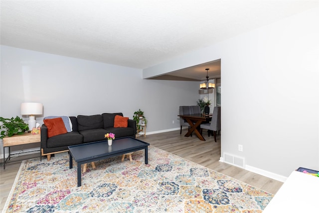 living room featuring light wood-style floors, baseboards, visible vents, and a textured ceiling