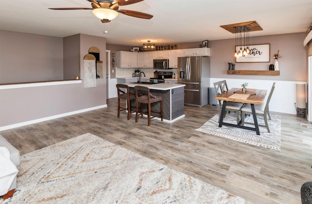 kitchen featuring light wood finished floors, stainless steel appliances, a kitchen island with sink, white cabinets, and a sink