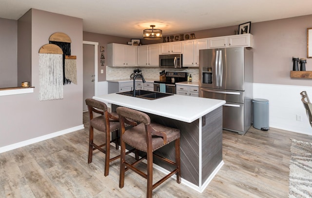 kitchen with light wood-style flooring, stainless steel appliances, light countertops, a kitchen bar, and a sink