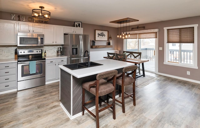 kitchen with light wood-style flooring, stainless steel appliances, a breakfast bar, a sink, and backsplash