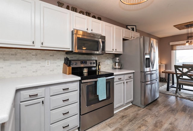 kitchen with appliances with stainless steel finishes, wood finished floors, light countertops, white cabinetry, and backsplash