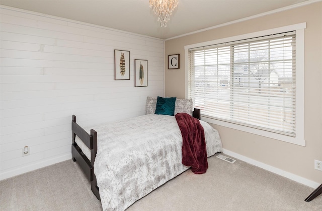 carpeted bedroom with wooden walls, visible vents, baseboards, ornamental molding, and an inviting chandelier