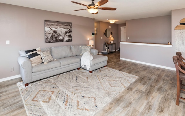 living room with ceiling fan, baseboards, and wood finished floors