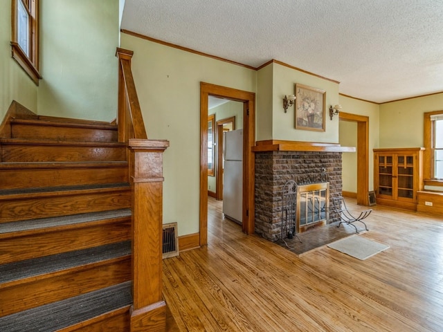 living area featuring visible vents, stairway, ornamental molding, a brick fireplace, and light wood-type flooring