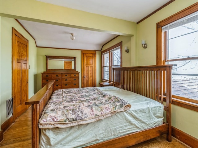 bedroom featuring ornamental molding, visible vents, baseboards, and wood finished floors