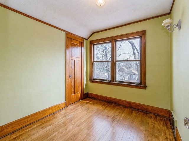 empty room featuring baseboards, lofted ceiling, light wood-style flooring, crown molding, and a textured ceiling