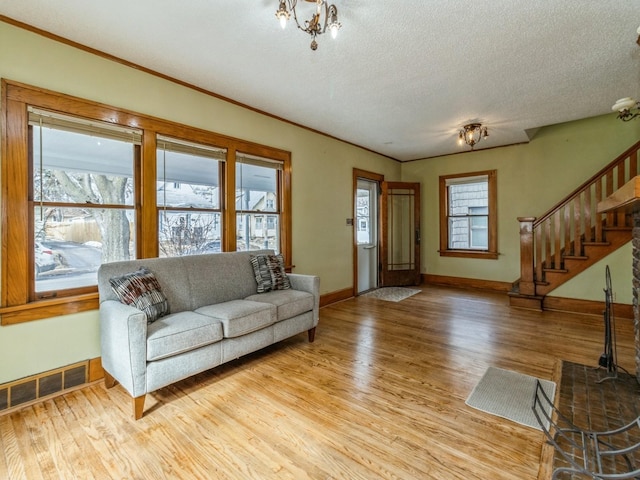 living area featuring light wood finished floors, baseboards, visible vents, stairway, and a textured ceiling