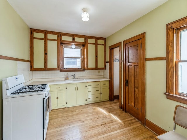 kitchen with light countertops, white gas stove, backsplash, and a sink