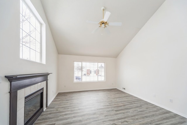 unfurnished living room with light wood-type flooring, a tile fireplace, a wealth of natural light, and baseboards