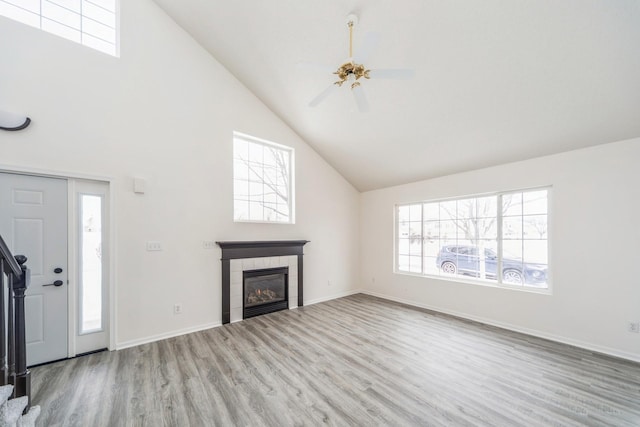 unfurnished living room with light wood-style floors, a wealth of natural light, high vaulted ceiling, and a tile fireplace