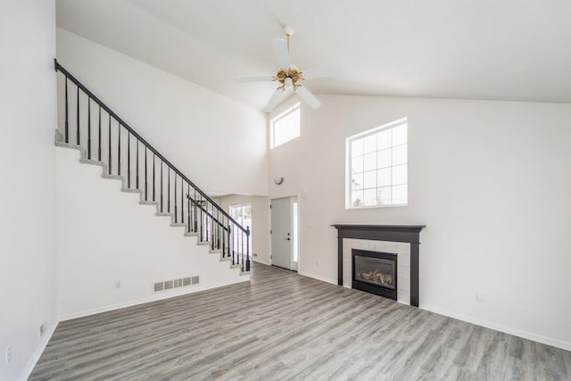 unfurnished living room featuring visible vents, a tiled fireplace, a ceiling fan, wood finished floors, and stairs