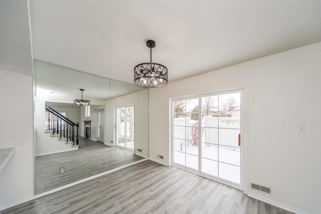 unfurnished living room with visible vents, an inviting chandelier, wood finished floors, baseboards, and stairs