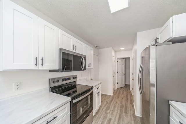 kitchen with light wood finished floors, white cabinetry, appliances with stainless steel finishes, and a textured ceiling