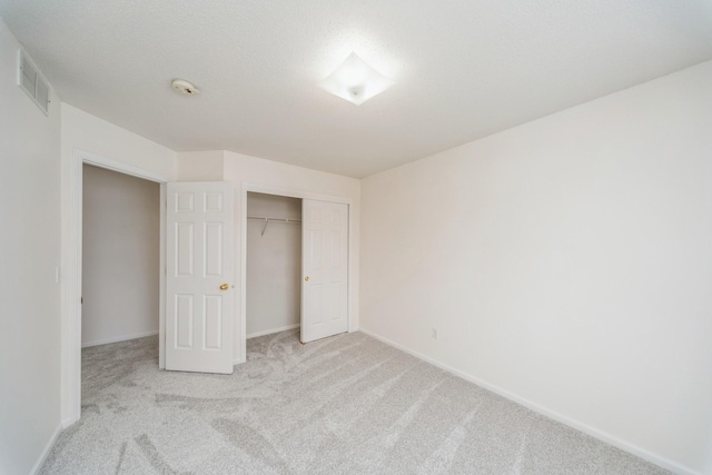 unfurnished bedroom featuring baseboards, visible vents, light colored carpet, a textured ceiling, and a closet