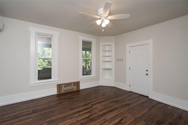 spare room featuring dark wood-style floors, built in shelves, ceiling fan, and baseboards