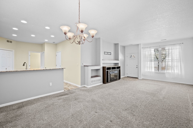 unfurnished living room with a fireplace with flush hearth, visible vents, a textured ceiling, and light colored carpet