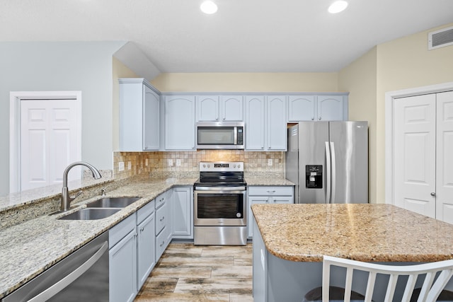 kitchen featuring visible vents, backsplash, appliances with stainless steel finishes, a sink, and light stone countertops