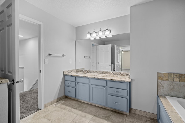 bathroom featuring double vanity, tiled bath, baseboards, a textured ceiling, and a sink