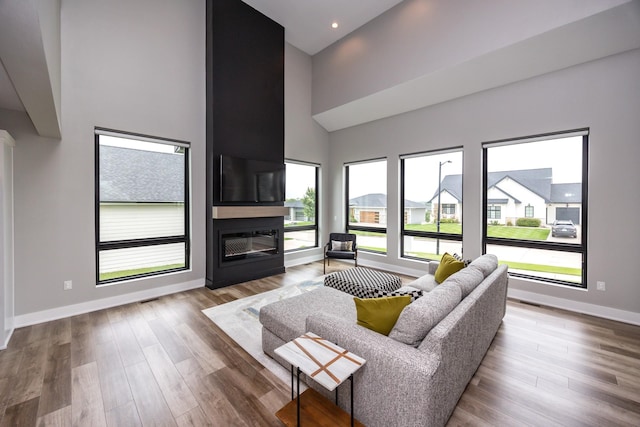 living area featuring baseboards, a fireplace, a high ceiling, and wood finished floors