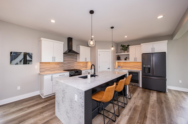 kitchen with white cabinets, wall chimney range hood, stainless steel gas range, open shelves, and black refrigerator with ice dispenser