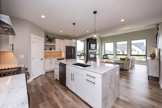 kitchen with appliances with stainless steel finishes, light stone counters, a kitchen island with sink, white cabinetry, and a sink