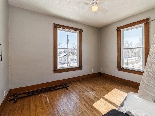 empty room with baseboards, ceiling fan, a textured ceiling, and light wood-style floors