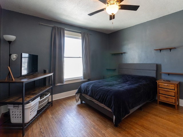 bedroom with a ceiling fan, a textured ceiling, baseboards, and wood finished floors