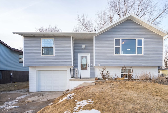 bi-level home with a garage, concrete driveway, and brick siding