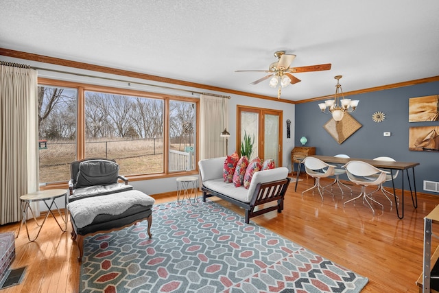 living area featuring a textured ceiling, ornamental molding, light wood-style flooring, and visible vents