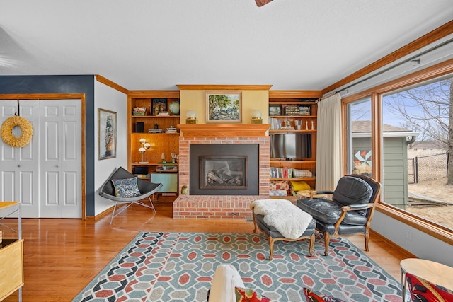 living room with built in shelves, a brick fireplace, baseboards, and wood finished floors