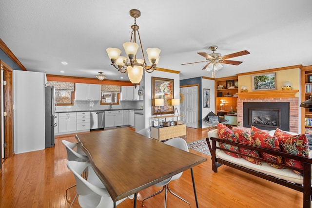 dining space with ceiling fan with notable chandelier, a fireplace, light wood-style flooring, and crown molding