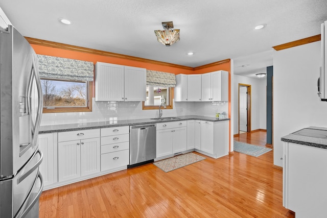 kitchen featuring stainless steel appliances, backsplash, light wood-style floors, white cabinetry, and a sink