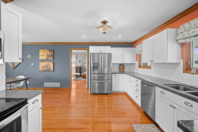 kitchen featuring visible vents, a sink, stainless steel appliances, light wood-style floors, and a wealth of natural light