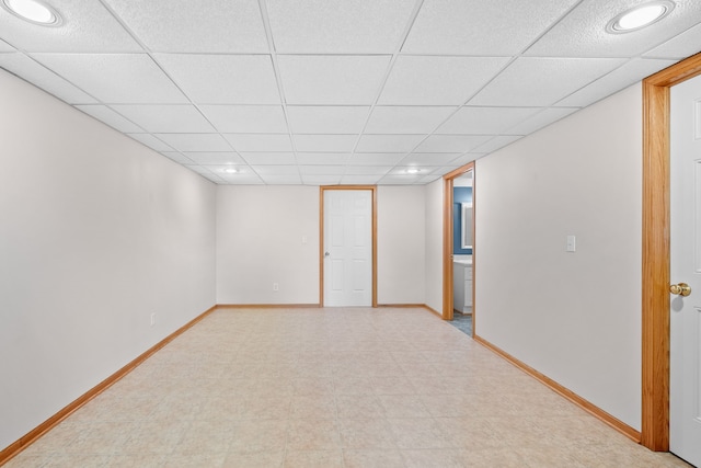 finished basement featuring baseboards, a drop ceiling, and tile patterned floors