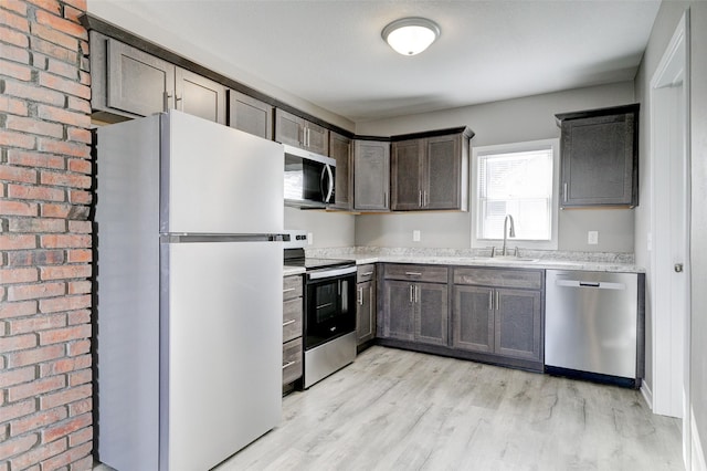 kitchen featuring dark brown cabinetry, appliances with stainless steel finishes, light stone countertops, light wood-type flooring, and a sink