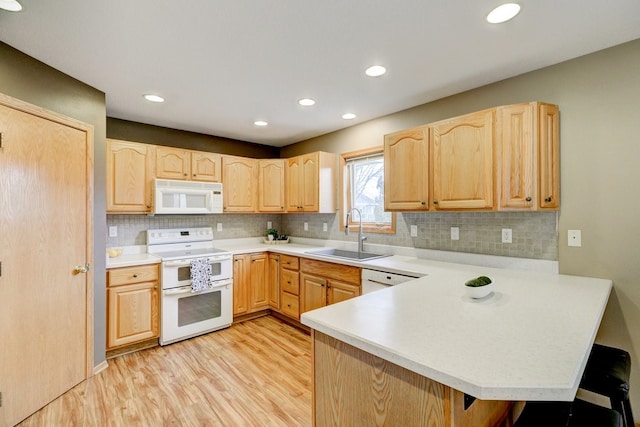 kitchen with light countertops, a sink, white appliances, a peninsula, and a kitchen breakfast bar