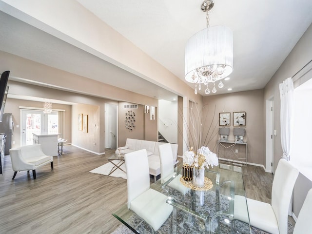 dining area with light wood finished floors, baseboards, visible vents, stairway, and an inviting chandelier