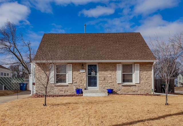 view of front facade with stone siding, roof with shingles, a front yard, and driveway