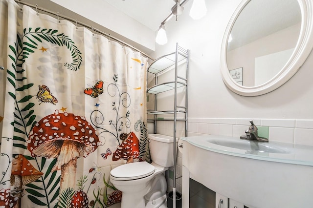 bathroom featuring tile walls, wainscoting, toilet, a shower with curtain, and a sink