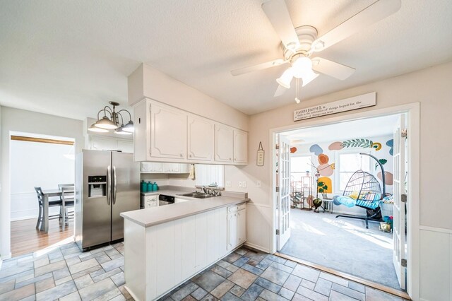 kitchen with stainless steel fridge, white cabinets, stone finish flooring, light countertops, and a sink