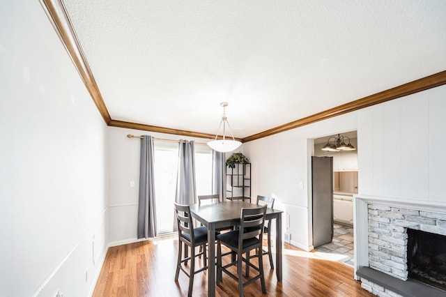 dining space with ornamental molding, a stone fireplace, a textured ceiling, and light wood-type flooring