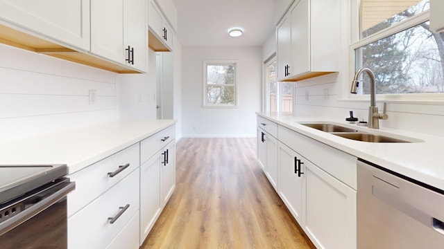 kitchen with light wood-type flooring, a sink, white cabinets, light countertops, and dishwasher